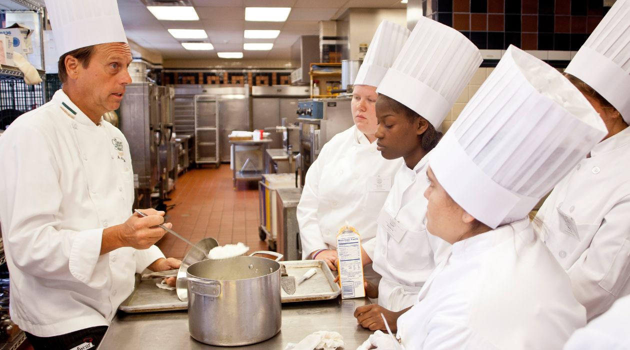 Culinary students in chefs uniforms and hats look on as an instructor leads a cooking demonstration at the Culinary Institute of America, Hyde Park